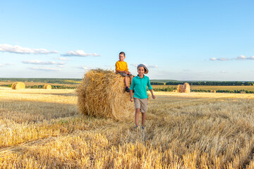 Children have fun  sit  on a haystack on a sunny day in the field.