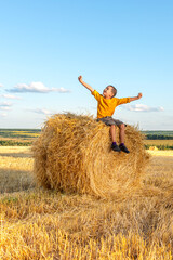 Young boy have fun  sit  on a haystack on a sunny day in the field.