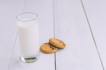 Oatmeal cookies with chocolate on a light background with a glass of milk.