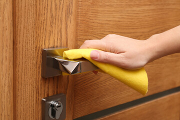 Woman cleaning door handle with rag indoors, closeup