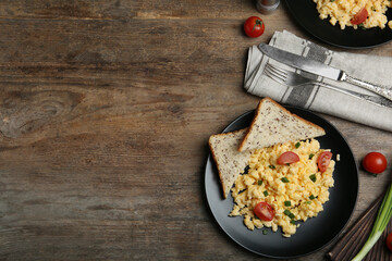 Tasty scrambled eggs served on wooden table, flat lay. Space for text