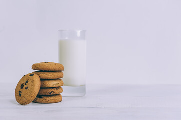 Oatmeal cookies with chocolate on a light background with a glass of milk.