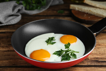 Tasty cooked chicken eggs with parsley in frying pan on wooden table, closeup