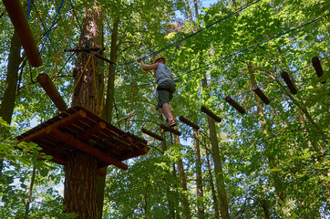 Fototapeta premium A boy with a helmet and insurance passes a high-altitude obstacle course.