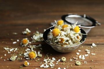 Dry chamomile flowers in infuser on wooden table, closeup