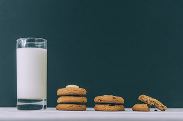 Oatmeal cookies with chocolate on a dark background with a glass of milk.