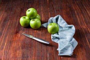High angle shot of some green apples and a knife and a tablecloth on a wooden surface