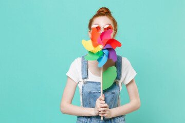 Funny young readhead girl in casual denim clothes eyeglasses posing isolated on blue turquoise wall...