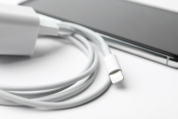 Smartphone and charging cable with adapter on white background, closeup