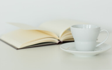 Open notebook with blank pages lying flat next to a coffee cup on a saucer. Isolated against white background. Calm study and relaxation. 