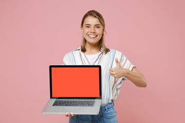 Smiling young blonde woman girl in casual striped shirt isolated on pink background. People lifestyle concept. Mock up copy space. Hold laptop pc computer with blank empty screen, showing thumb up.