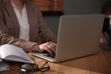 Woman working with laptop at wooden desk indoors, closeup