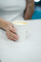 vista sobre hombro de mano sujetando cafe para llevar en cafeteria moderna