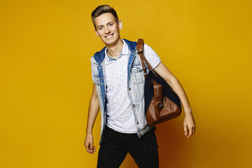 A young man in denim clothes is preparing his travel suitcase to give it into the luggage, isolated at the yellow background. Mockup of travel advertise