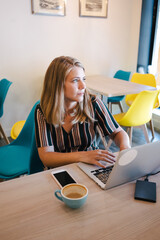 joven chica rubia europea pensativa en una cafetería con portátil en la mesa