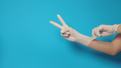 The hand is wearing white surgical gloves or latex gloves on a blue or Turquoise background.