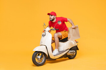 Delivery man in red cap t-shirt uniform driving moped motorbike scooter hold craft paper packet with food isolated on yellow background studio Guy employee working courier Service quarantine concept