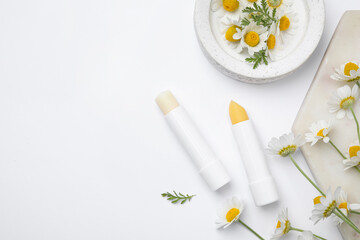 Fototapeta na wymiar Hygienic lipsticks and chamomile flowers on white background, top view