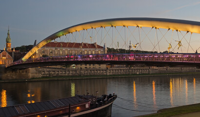Obraz premium Father Bernatek Footbridge lit up at sunset with the Vistula River in Krakow, Poland