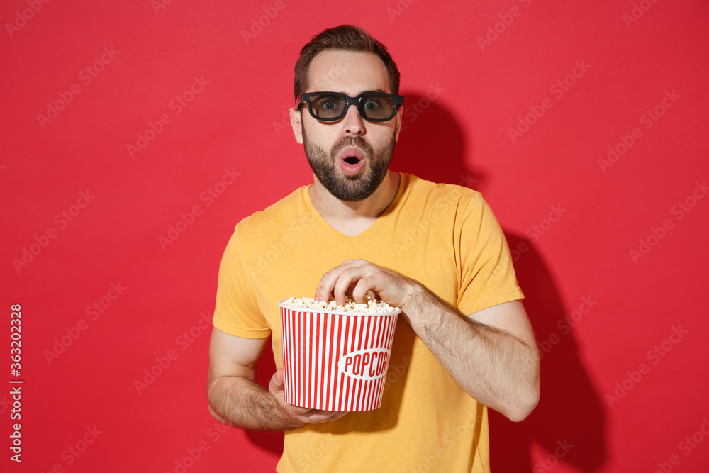 Wall mural amazed young bearded man guy in casual yellow t-shirt 3d glasses isolated on red wall background stu