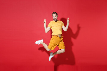 Fototapeta na wymiar Excited young bearded man guy in casual yellow t-shirt posing isolated on red background studio portrait. People sincere emotions lifestyle concept. Mock up copy space. Jumping showing victory sign.