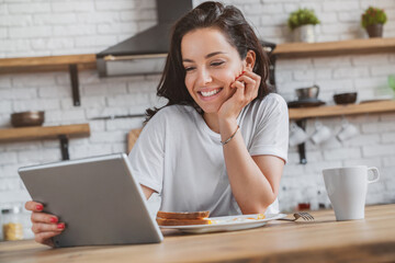 Woman using a tablet computer while drinking tea with breakfast in her kitchen