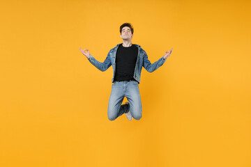 Fototapeta na wymiar Relaxed young man guy 20s wearing casual denim clothes posing isolated on yellow wall background. People lifestyle concept. Mock up copy space. Jumping hold hands in yoga gesture, relaxing meditating.