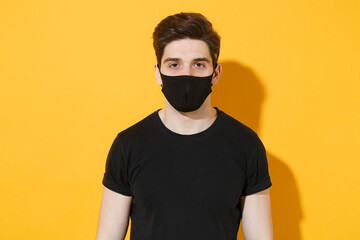 Handsome young guy in casual black t-shirt face mask posing isolated on yellow background studio...