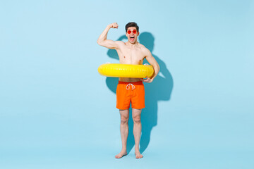 Excited young man in orange shorts glasses hold inflatable ring isolated on blue background studio portrait. People summer vacation rest lifestyle concept. Mock up copy space. Showing biceps, muscles.