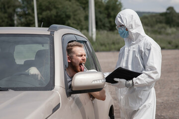 Doctor in protective virus suit taking swab from person driver to test for COVID-19 coronavirus infection