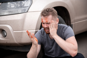 Young man sits with bloodied head near wheel of car, screaming and regretting act