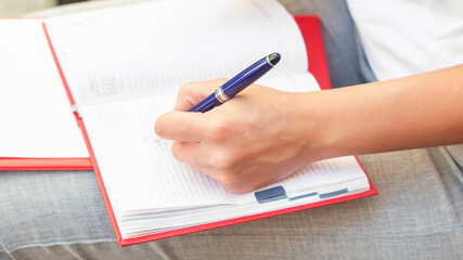 close up of female hand is writing plans to the notebook outdoor, girl's hand writes in notebook outside