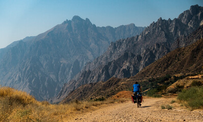 Cycle traveler on a dirt road with large mountains in the background