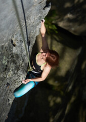 Brave lady mountaineer in sportswear using rope while climbing alpine ridge. Young woman ascending mountain and trying to reach mountaintop. Concept of mountaineering, alpinism and alpine climbing.