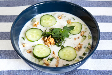 Blue plate with tarator on a striped tablecloth. Cold soup with cucumbers.