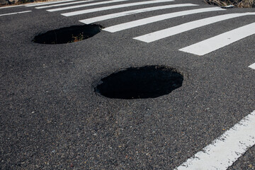 Dangerous deep holes on an asphalt highway near a pedestrian crossing. Danger of injury