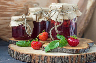 Strawberry jam in jars on a wooden board and a tray with strawberries and basil, rustic style, horizontal