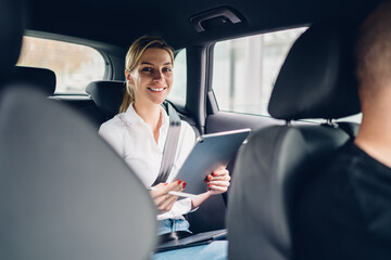 Fototapeta na wymiar Portrait of positive female economist working with accounting via modern touch pad and smiling at camera during car trip to meeting, happy successful businesswoman with tablet for digital marketing