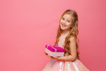 a little girl in a beautiful dress holds a gift on a pink background, celebrating her birthday