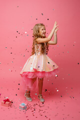 happy Little girl catches confetti on pink background, holiday concept