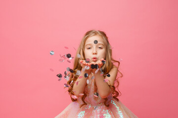 a little girl in an elegant dress blows confetti on a pink background, holiday concept