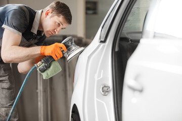 Man grinds white car after painting, auto repair shop.