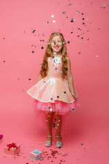 happy Little girl catches confetti on pink background, holiday concept