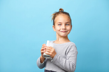Beautiful little girl with glass of milk, stands on blue isolated.