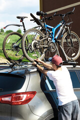 Fototapeta na wymiar Man is fixing bicycles on the roof of a car on a summer sunny day for transportation