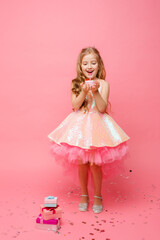 baby girl in pink dress celebrates birthday with cake on pink background