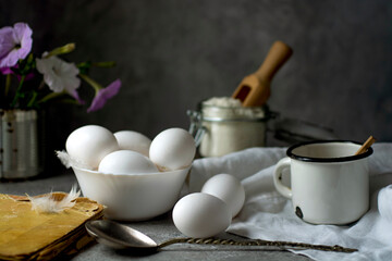 Chicken eggs, flour, milk and an old recipe book on the kitchen table.