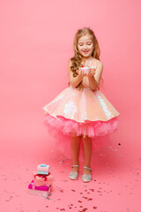 baby girl in pink dress celebrates birthday with cake on pink background
