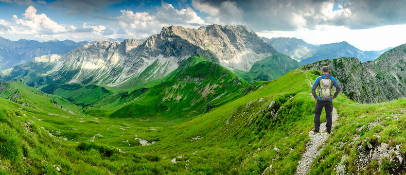 Hiker Man on Hiking Trail with Backpack standing relaxed and enjoying panoramic view to mountains. Alps, Hohe Gaenge, Allgau, Bad Hindelang, Hinterstein, Bavaria, Germany.