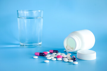 Close up of teblets pills with pill bottle and a glass of water on blue background 